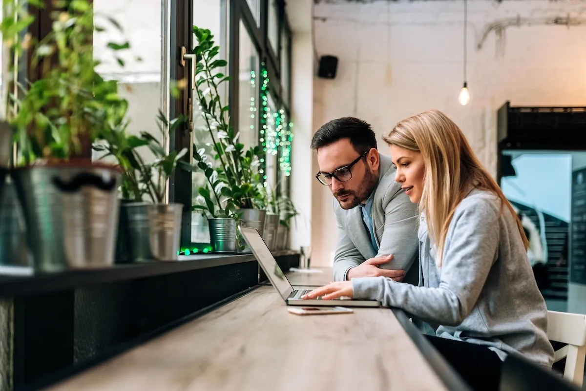 Two people sitting behind a table and a laptop, observing.